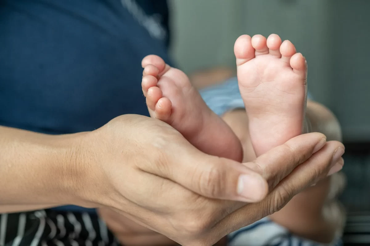 Imagem de uma das mãos de uma mãe segurando os pés do bebê, enquanto aguarda o médico para realizar o teste do pezinho